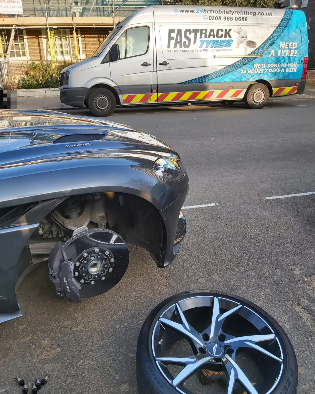 Aston Martin DBS Superleggera with the wheel off and carbon-ceramic brake exposed during a mobile tyre change
