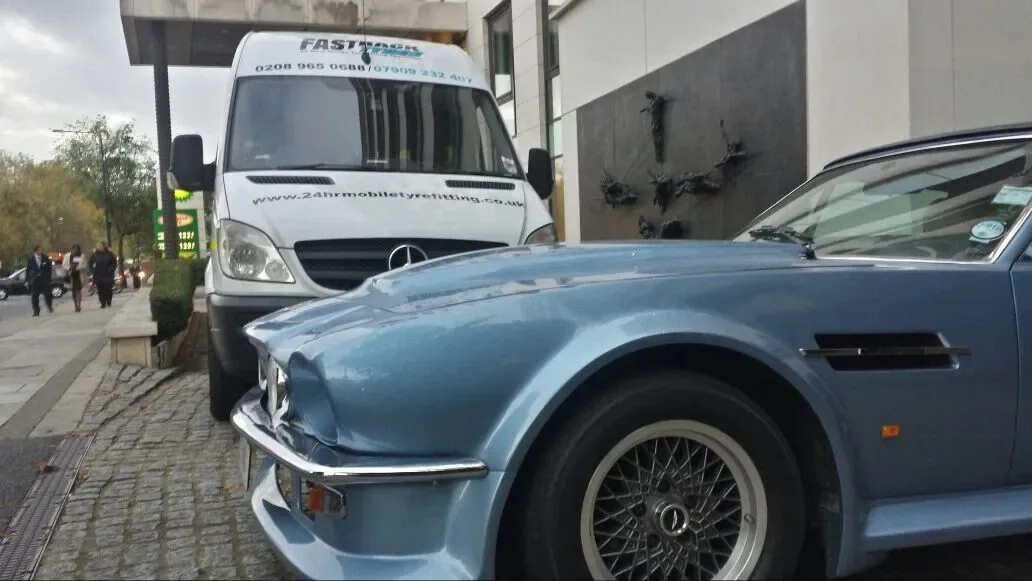 Classic blue Aston Martin V8 attended kerbside by the Fastrack heritage van