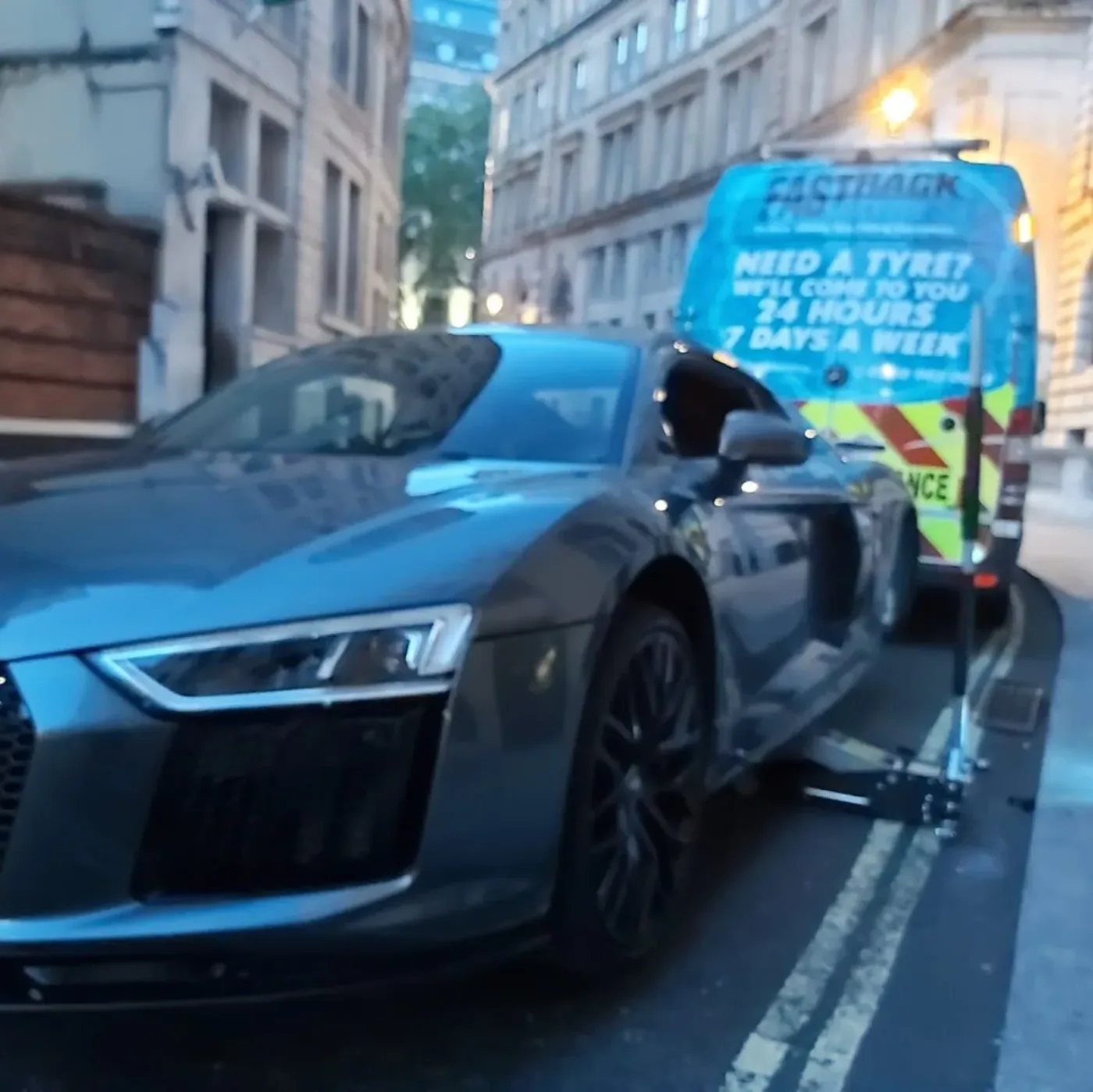 Grey Audi R8 having a tyre replaced beside the Fastrack van