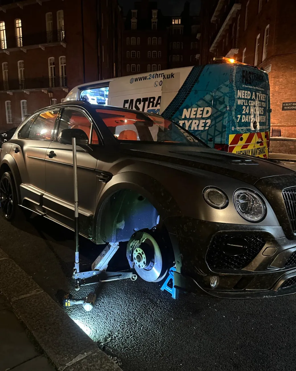 Matte-black Bentley Bentayga wheel-off tyre change at night in Kensington