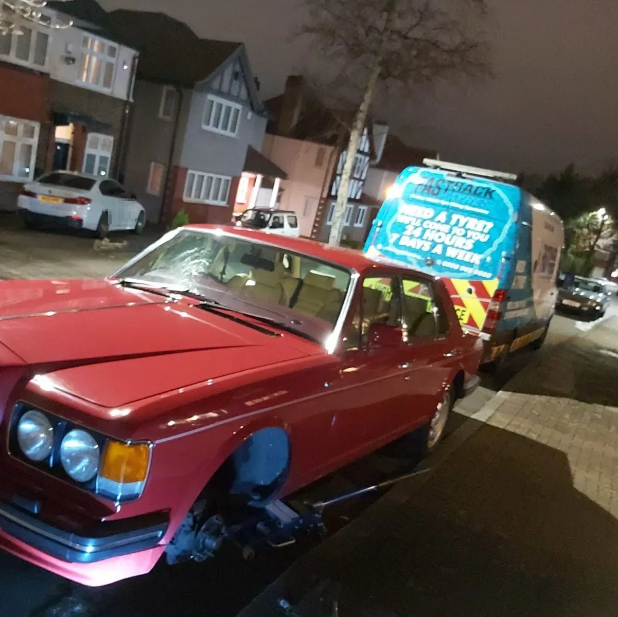 Red classic Bentley saloon with its front wheel removed at night and the Fastrack Tyres van behind