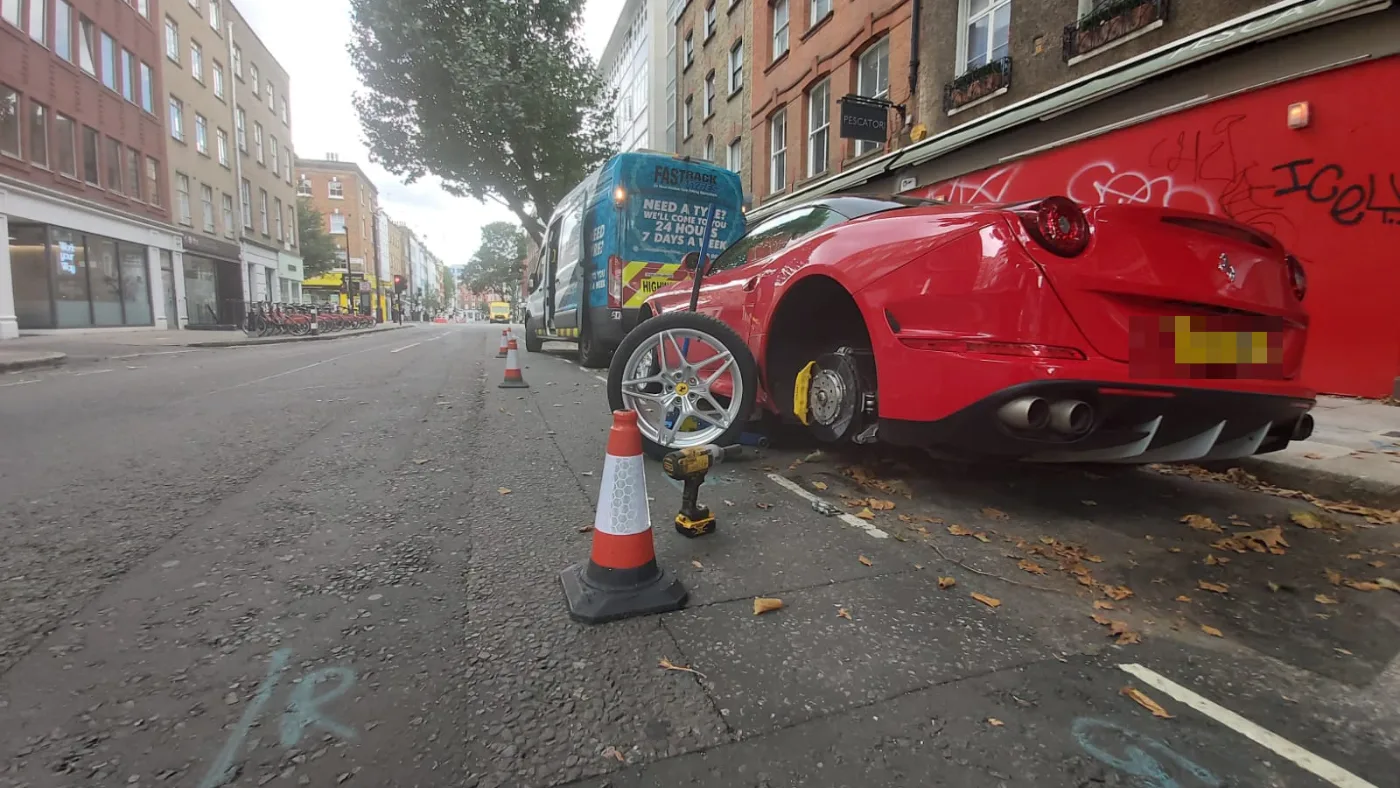 Red Ferrari California with a wheel off during a roadside mobile tyre change in London