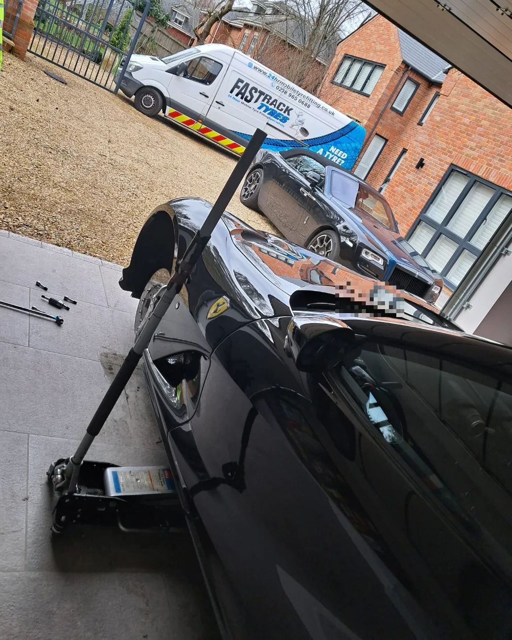 Ferrari with the front wheel removed on a private driveway, Rolls-Royce alongside