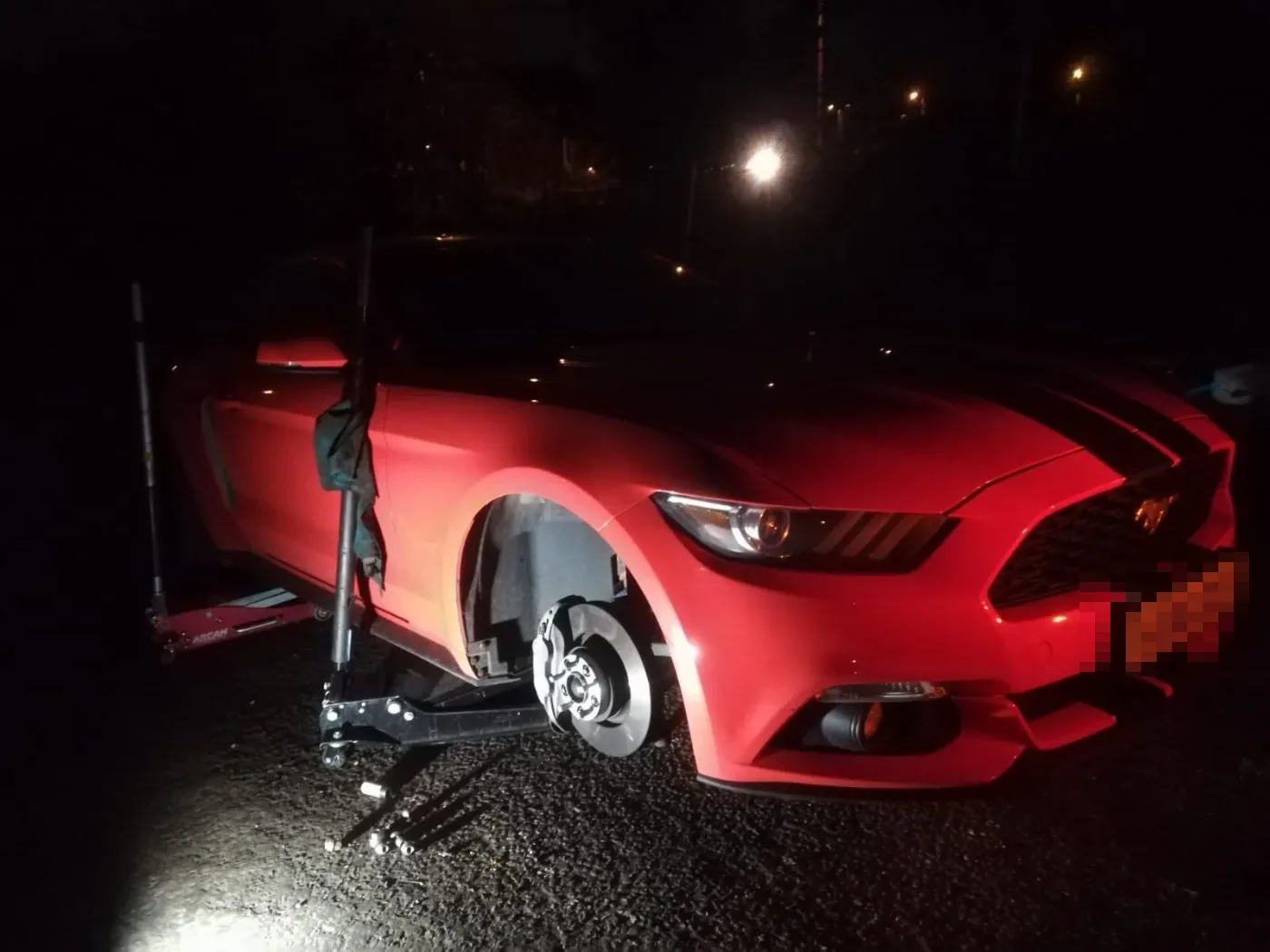Red Ford Mustang with a wheel off during a night tyre change