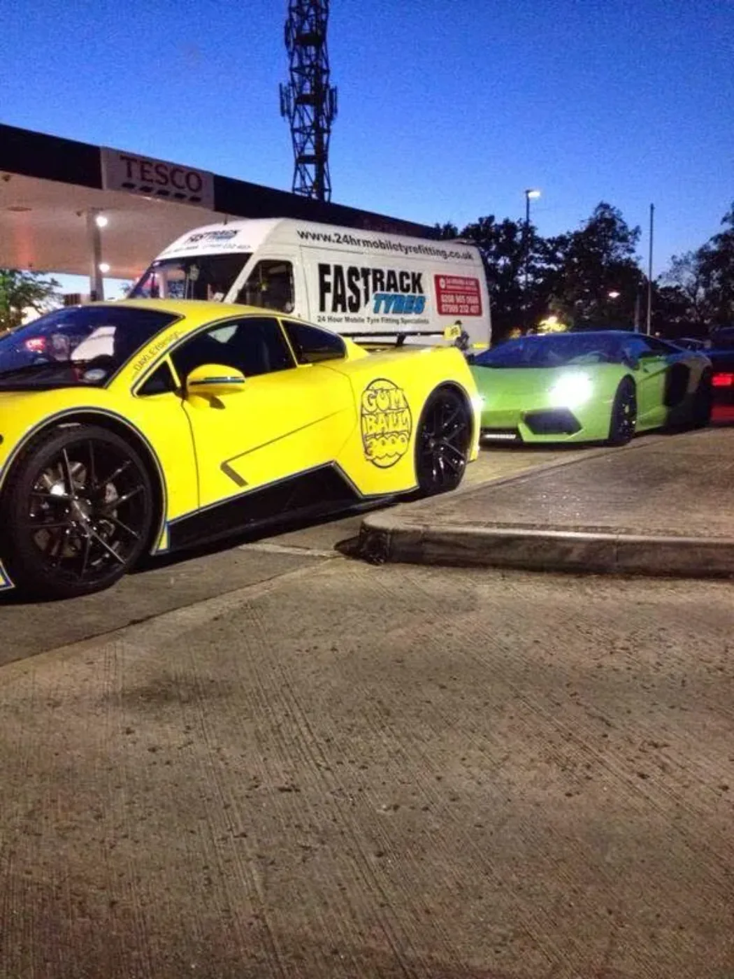 Yellow Gumball-liveried supercar beside a green Lamborghini Gallardo at a petrol-station forecourt with the Fastrack van behind