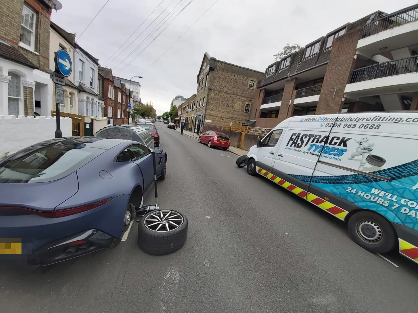 Blue Jaguar F-Type having a wheel changed on a London street beside the Fastrack van