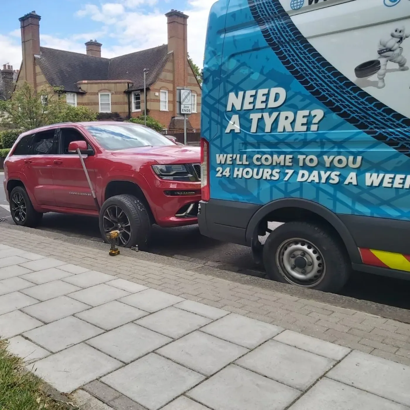 Red Jeep Grand Cherokee having a wheel changed beside the Fastrack van