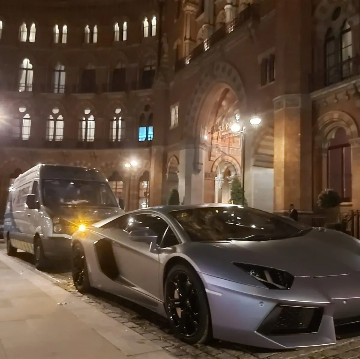 Silver Lamborghini Aventador beside the Fastrack Tyres van outside St Pancras at night