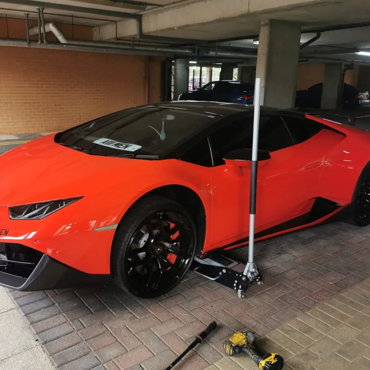Orange Lamborghini Huracan raised on a trolley jack for a mobile tyre change in a car park