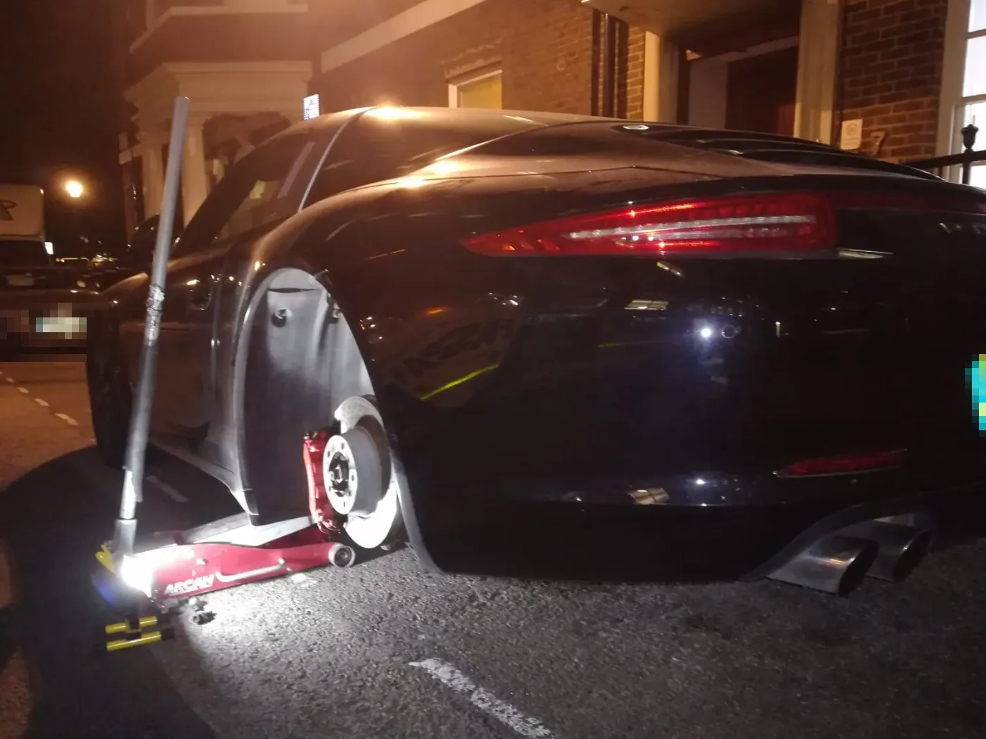 Black Maserati GranTurismo having a rear wheel changed at night outside a venue