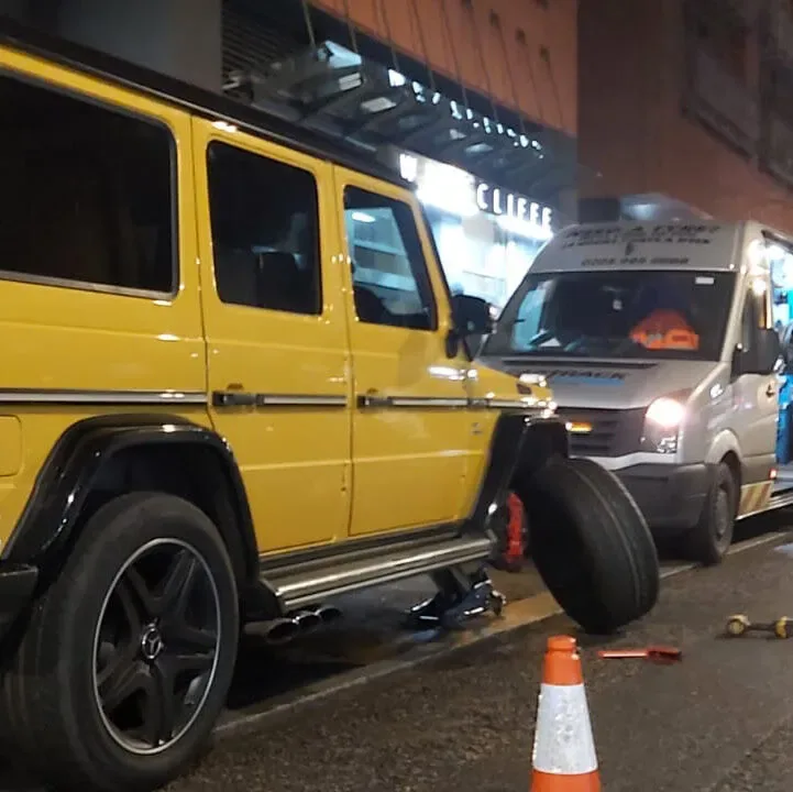 Yellow Mercedes G-Wagon having a wheel changed at night beside the Fastrack van