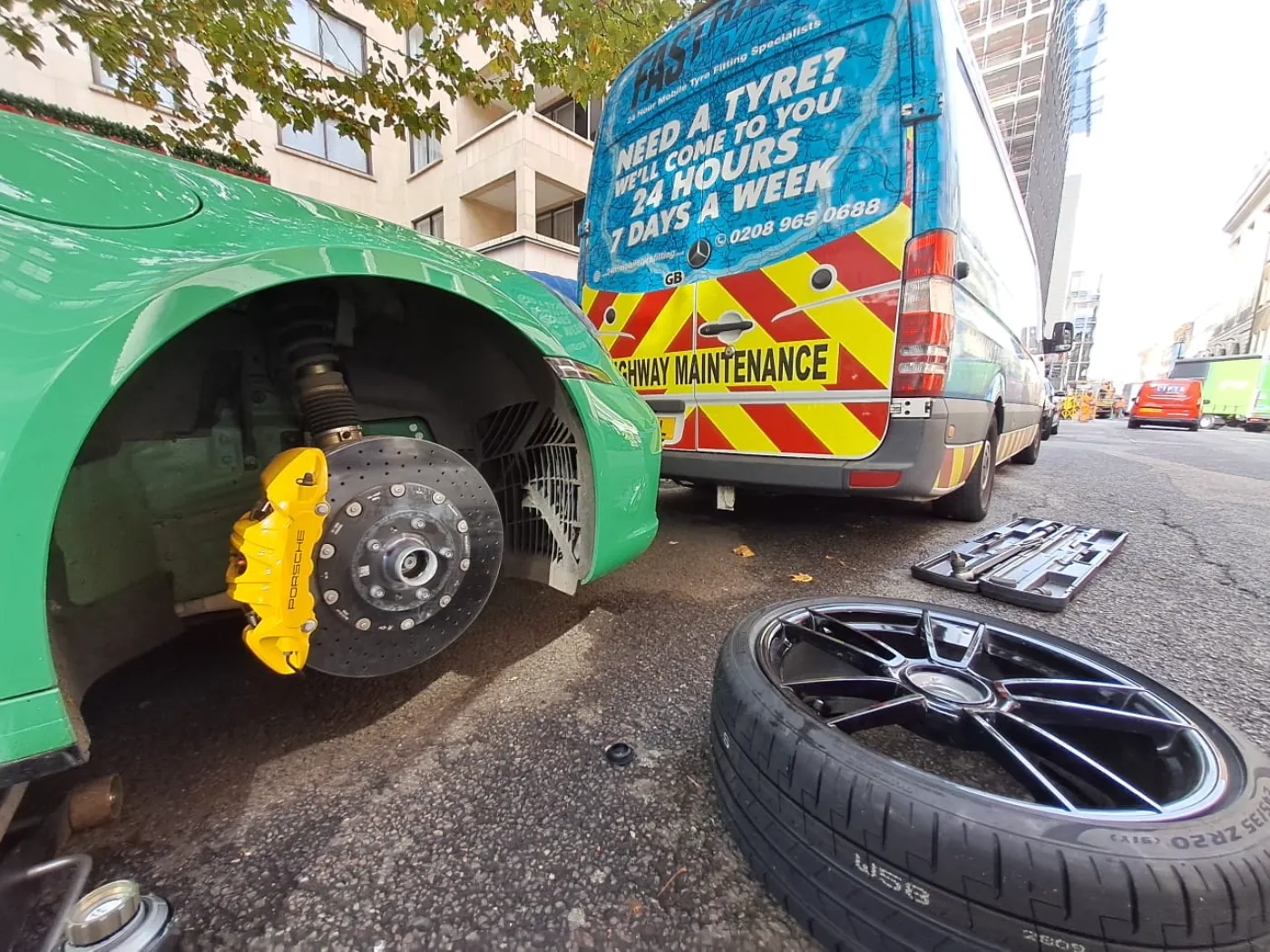 Green Porsche 911 with carbon-ceramic brakes during a mobile tyre change