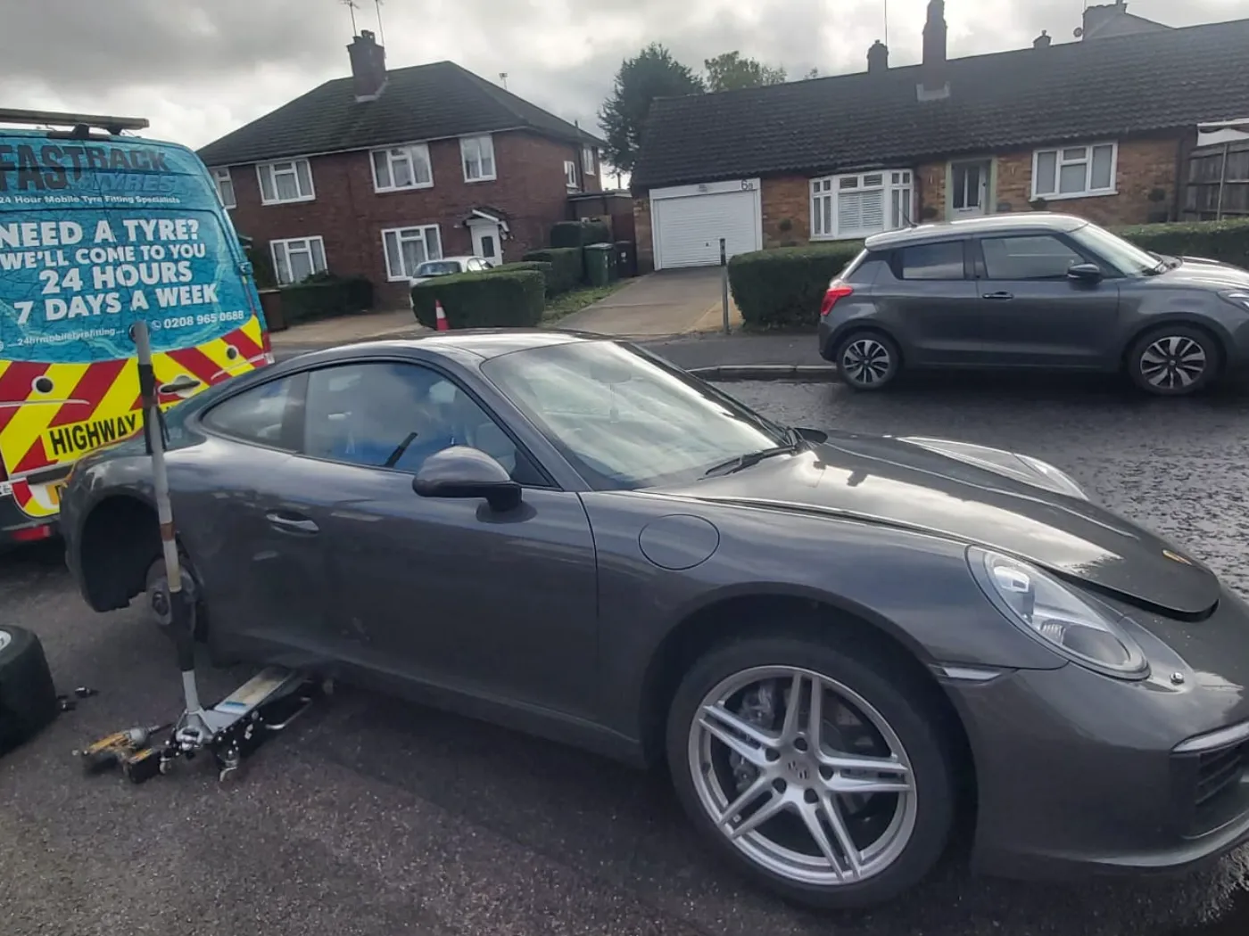 Grey Porsche 911 having a wheel changed on a suburban street