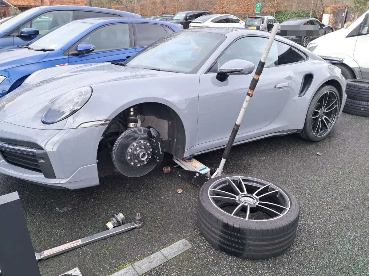 Porsche 911 Turbo S with the front wheel off for a mobile tyre change in a London car park