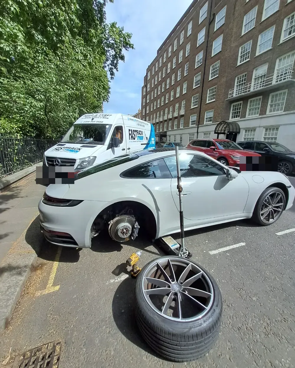 White Porsche 911 having a tyre replaced kerbside in central London by the Fastrack van