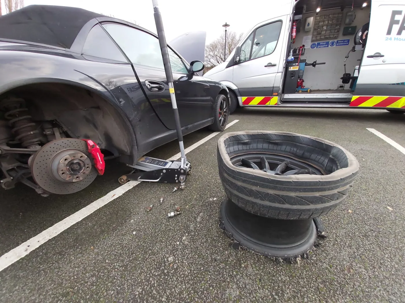 Deflated run-flat tyre off the alloy beside a Porsche during an emergency mobile tyre replacement, Fastrack van workshop open