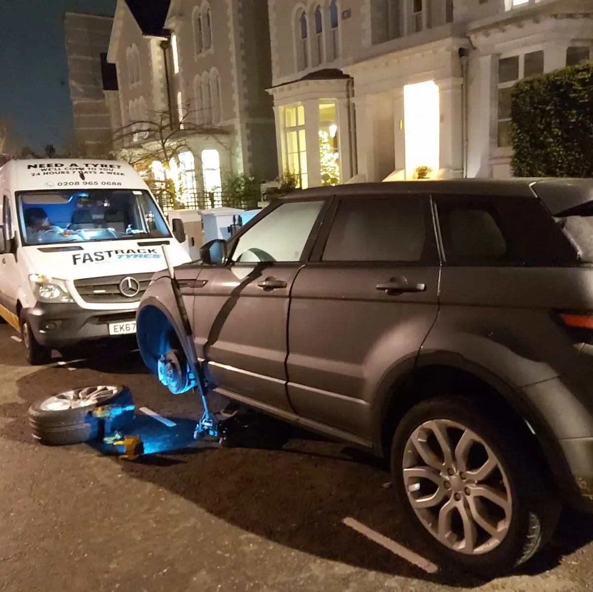 Grey Range Rover Evoque having a wheel changed at night outside a London villa