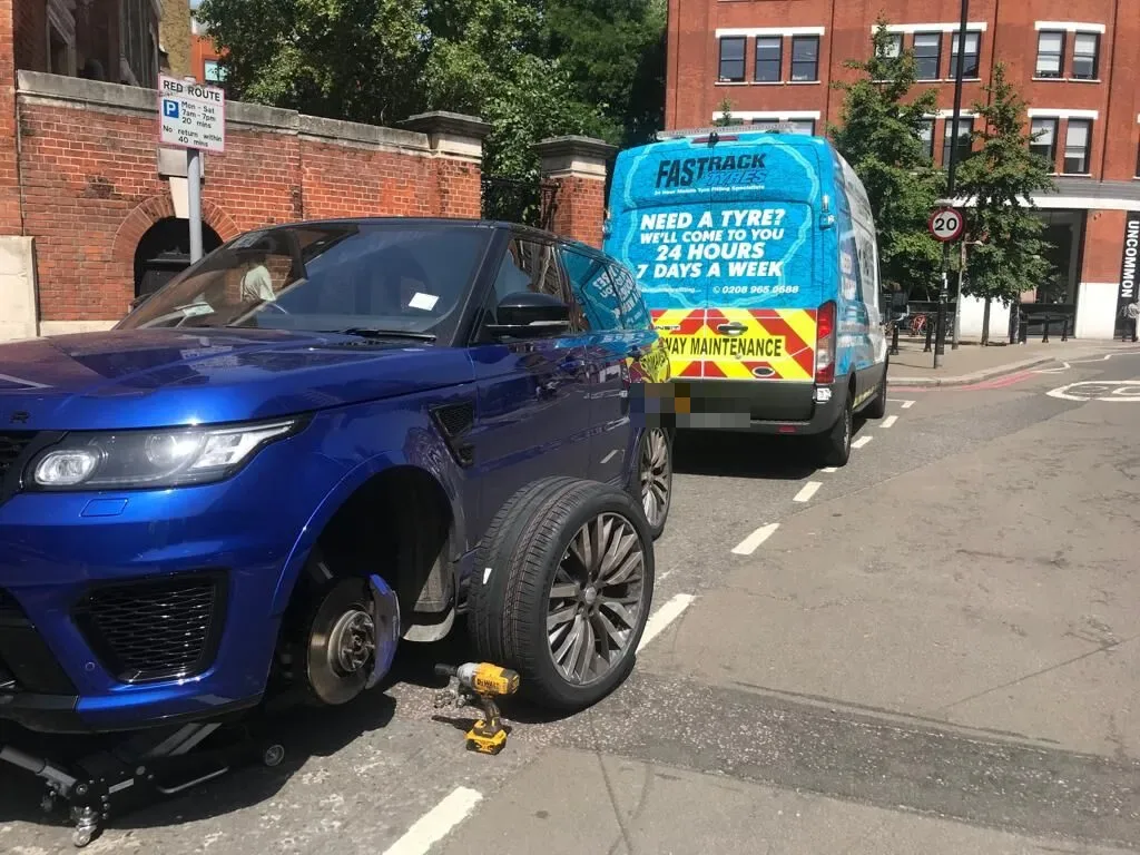 Blue Range Rover Sport SVR having a front wheel changed on a red-route street with the Fastrack Tyres van behind