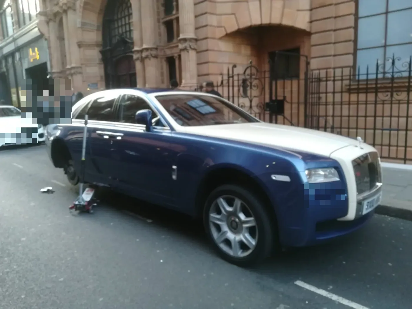 Two-tone blue and silver Rolls-Royce Ghost having a wheel changed on a grand London street