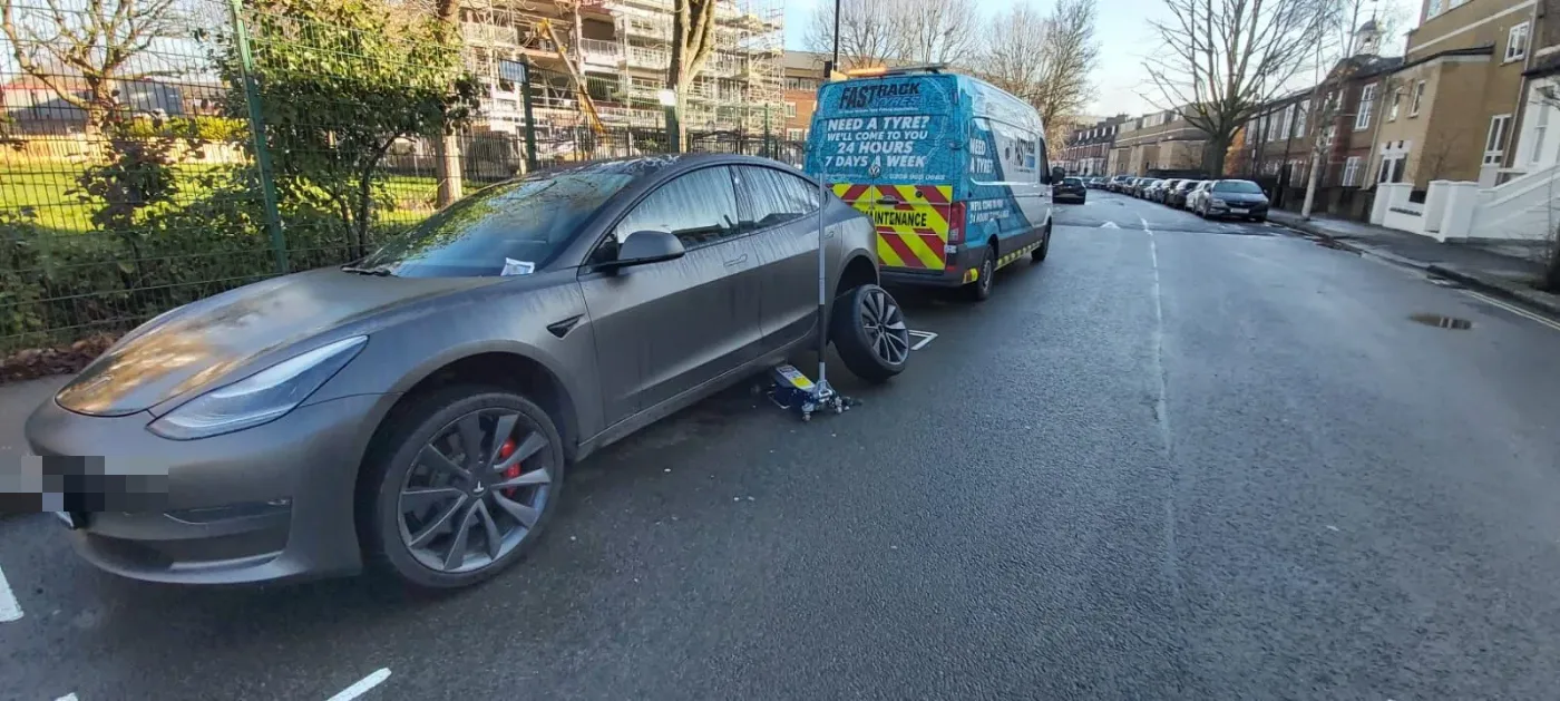 Grey Tesla Model 3 having a wheel changed on a wet London street with the Fastrack Tyres van behind