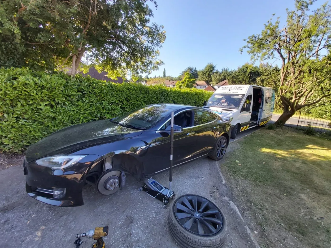 Black Tesla Model S with its front wheel removed on a grass verge with the Fastrack Tyres van behind