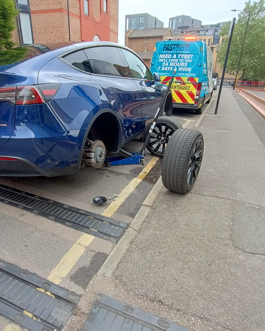 Blue Tesla Model Y with a wheel off for a mobile tyre replacement
