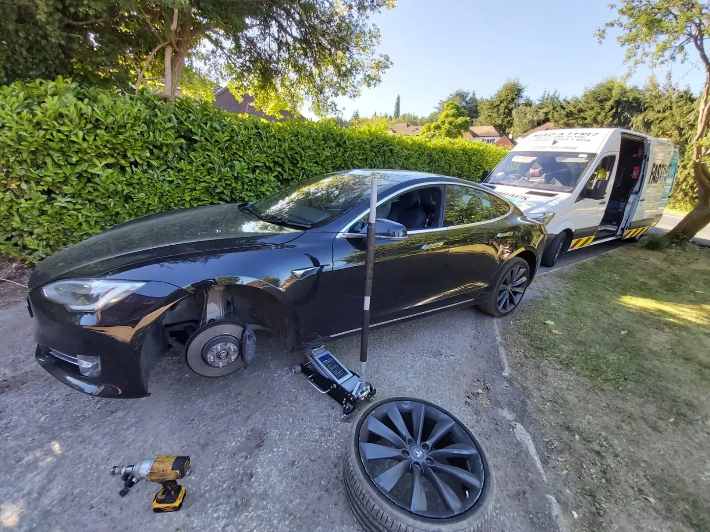 Black Tesla Model S having a wheel changed on a driveway