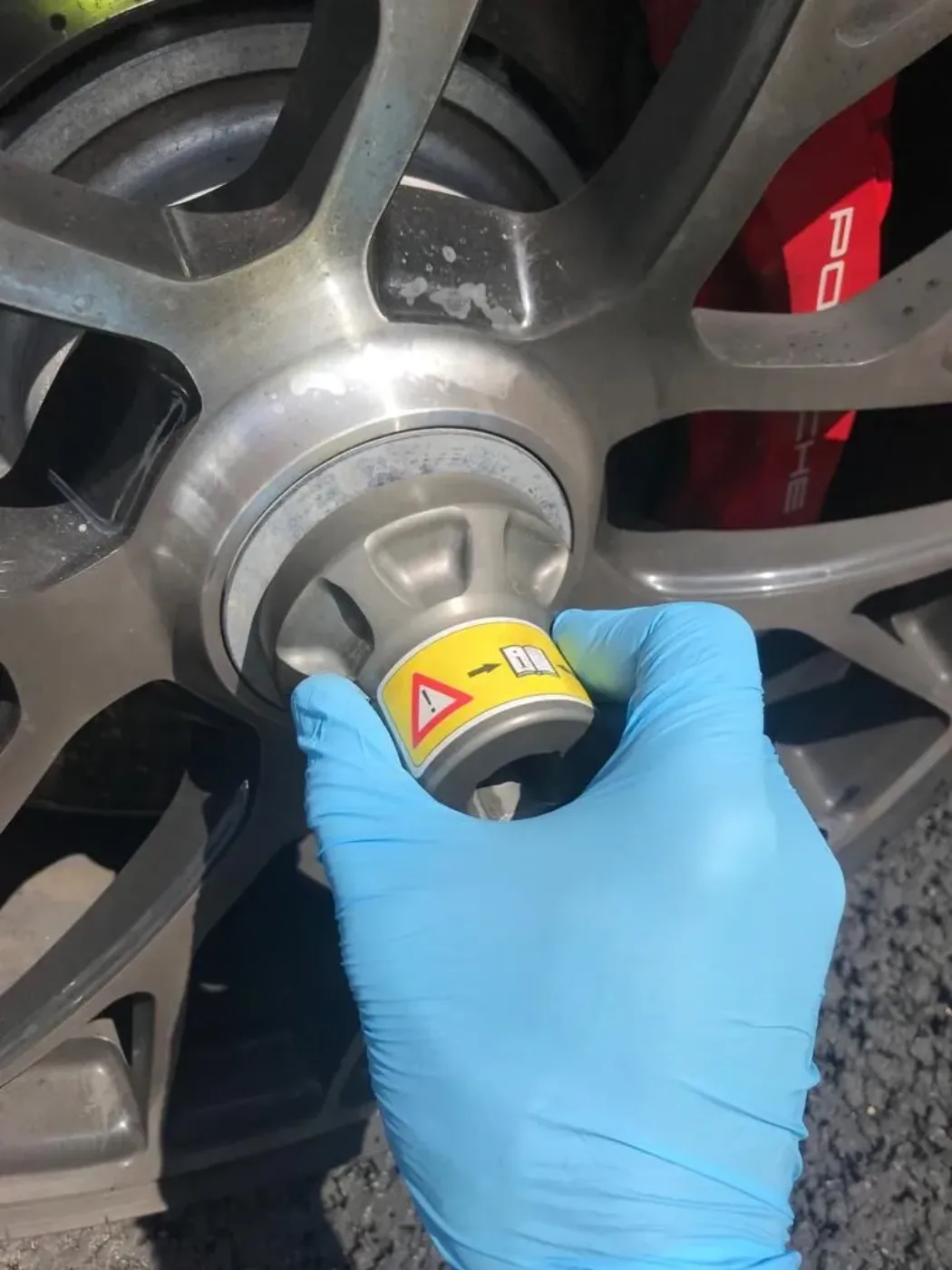 Gloved technician torquing a wheel nut on a Porsche with red calipers